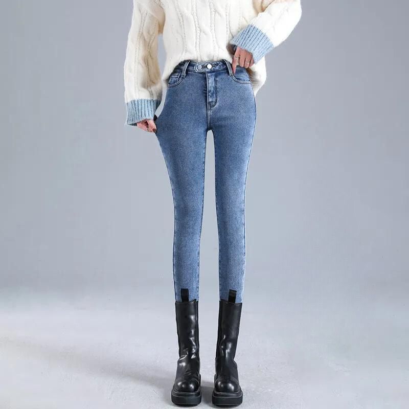 IMG_11_2023_pantalon_polaire_femme_style_jean_double_beige (2) Mannequin debout devant un mur gris, portant un jean slim bleu, avec des bottes à lacets et un pull blanc.