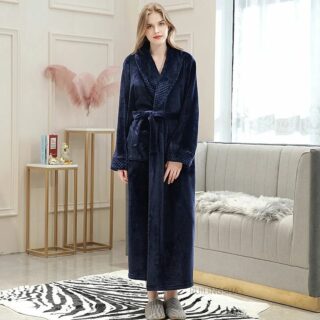 Mannequin femme debout sur un tapis zèbre, avec un canapé gris derrière elle et un mur beige avec des moulures. Elle porte un peignoir monochrome bleu foncé et des chaussons gris clair. Elle a les bras le long du corps.