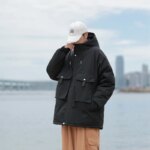 Manteau polaire homme chaude et à capuche, de couleur noir, avec deux grosse poches devant, porté par un homme avec casquette blanche et pantalon marron