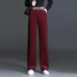 Mannequin debout devant un fond marron, portant un pantalon en velours rouge, avec une taille élastique et deux poches, et des baskets blanches.