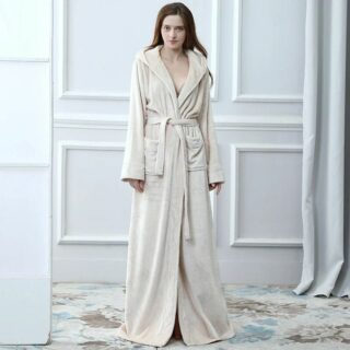 Mannequin femme de face, avec une mur blanc avec des moulures derrière elle, portant un peignoir beige fermé par une ceinture, extra long, on ne voit pas ses pieds.