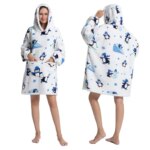 Mannequin debout sur un fond blanc, portant un poncho avec des manches longues, une capuche et une poche centrale kangourou. Le poncho est blanc avec des motifs pingouins bleus. À droite la mannequin et de face et à gauche elle est de dos.