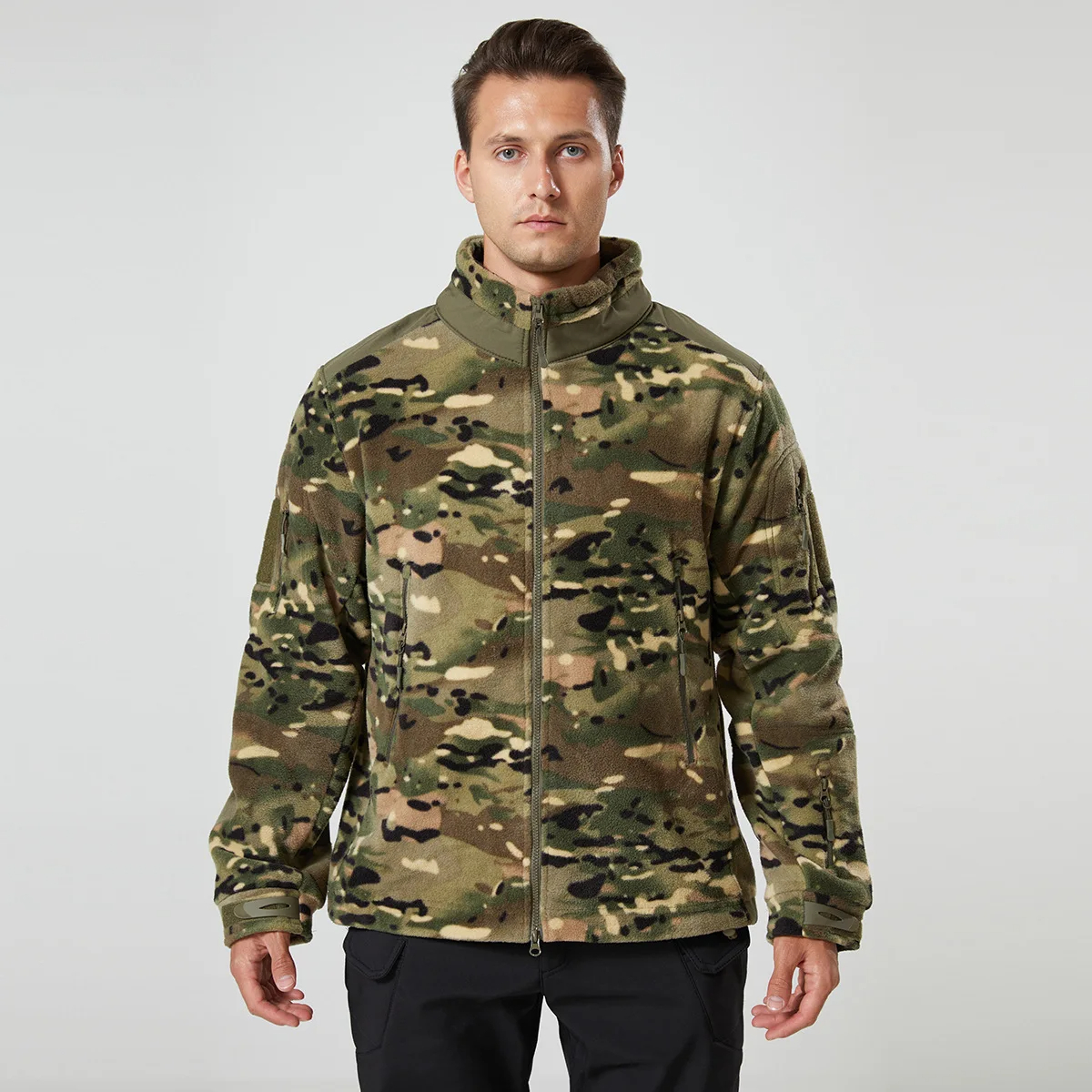 Veste polaire homme à col montant imprimé camouflage porté par un homme avec un pantalon noir sur fond gris